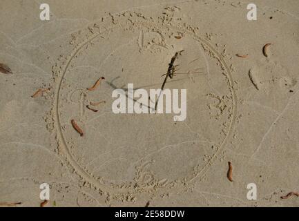 Handgezeichnete Uhr mit Zahlen im Sand mit einem Ein Stück Gras, um es in eine Sonnenuhr zu verwandeln Stockfoto