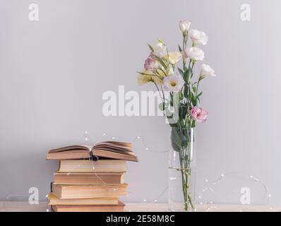Eustoma blumen blumenstrauss in der Vase, der Alten vintage Bücher und girlande Lichter auf grauem Hintergrund. Lesen und Konzept entspannen Stockfoto