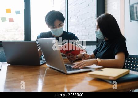 Asiatische Frau und Mann Arbeitnehmer treffen zusammen mit Laptop für Finanzielle und tragen Schutzmasken verhindern Corona-Virus oder covid19 Im CO-Arbeitsbereich Stockfoto