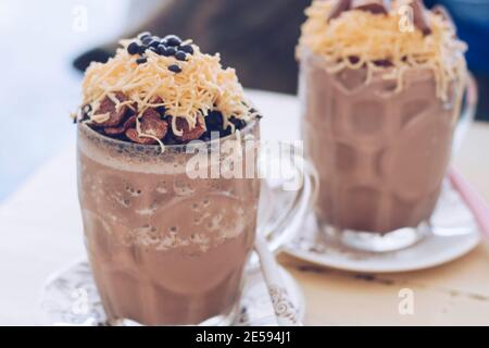 Schokoladen-Milchshake mit Schokoladengetreide, Käse und Schoko-Chips in der großen Klarglas-Tasse. Selektive Nahaufnahme und verschwommenes Backg Stockfoto