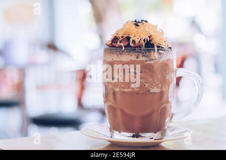 Schokoladen-Milchshake mit Schokoladengetreide, Käse und Schoko-Chips in der großen Klarglas-Tasse. Selektive Nahaufnahme und verschwommenes Backg Stockfoto