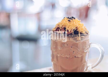 Schokoladen-Milchshake mit Schokoladengetreide, Käse und Schoko-Chips in der großen Klarglas-Tasse. Selektive Nahaufnahme und verschwommenes Backg Stockfoto