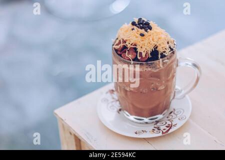 Schokoladen-Milchshake mit Schokoladengetreide, Käse und Schoko-Chips in der großen Klarglas-Tasse. Selektive Nahaufnahme und verschwommenes Backg Stockfoto