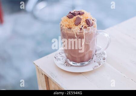 Schokoladen-Milchshake mit Schokoladengetreide, Käse und Schoko-Chips in der großen Klarglas-Tasse. Selektive Nahaufnahme und verschwommenes Backg Stockfoto