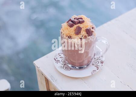 Schokoladen-Milchshake mit Schokoladengetreide, Käse und Schoko-Chips in der großen Klarglas-Tasse. Selektive Nahaufnahme und verschwommenes Backg Stockfoto