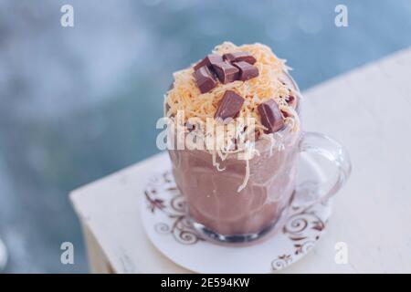 Schokoladen-Milchshake mit Schokoladengetreide, Käse und Schoko-Chips in der großen Klarglas-Tasse. Selektive Nahaufnahme und verschwommenes Backg Stockfoto