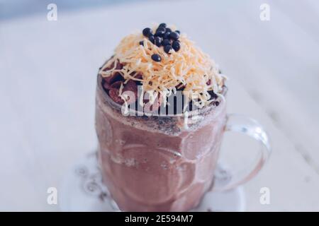 Schokoladen-Milchshake mit Schokoladengetreide, Käse und Schoko-Chips in der großen Klarglas-Tasse. Selektive Nahaufnahme und verschwommenes Backg Stockfoto