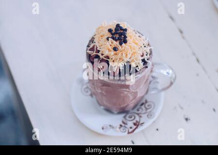 Schokoladen-Milchshake mit Schokoladengetreide, Käse und Schoko-Chips in der großen Klarglas-Tasse. Selektive Nahaufnahme und verschwommenes Backg Stockfoto