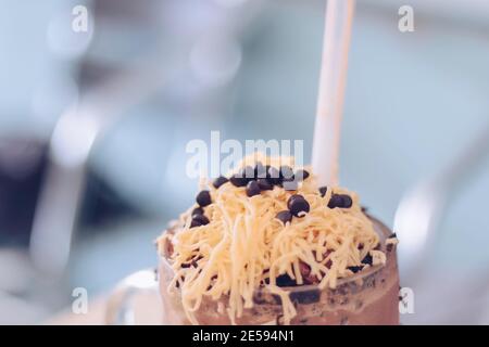 Schokoladen-Milchshake mit Schokoladengetreide, Käse und Schoko-Chips in der großen Klarglas-Tasse. Selektive Nahaufnahme und verschwommenes Backg Stockfoto