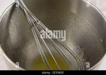 Metallbesen in Edelstahl-Rührschüssel mit letzten kleinen Rest Von Zitrone Dessert Belag Stockfoto