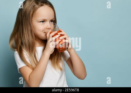 Glücklich lächelnd nettes Kind Mädchen in weißen T-Shirt Getränke genießt Frischer Fruchtsaft und Blick auf den Kopierplatz Stockfoto