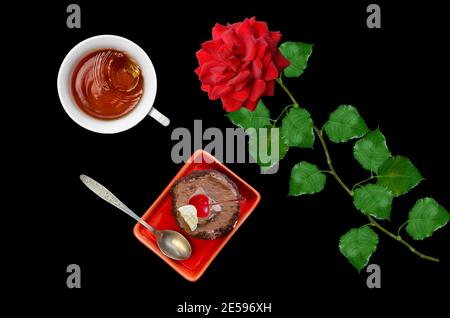 Kirschkuchen, eine Rose und eine Tasse Tee auf schwarzem Hintergrund. Der Blick von oben Stockfoto