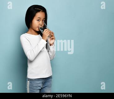Asiatisch koreanisch Kind Mädchen in Jeans und weiß lange Ärmel shirt steht trinkbares reines Wasser aus Glas am Kopierplatz Stockfoto
