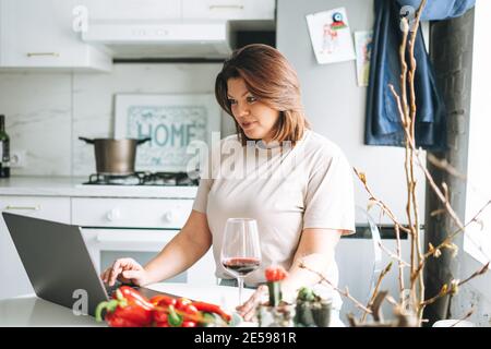 Schöne lächelnde Brünette junge Frau plus Größe Körper positiv mit Laptop in der Küche zu Hause Stockfoto