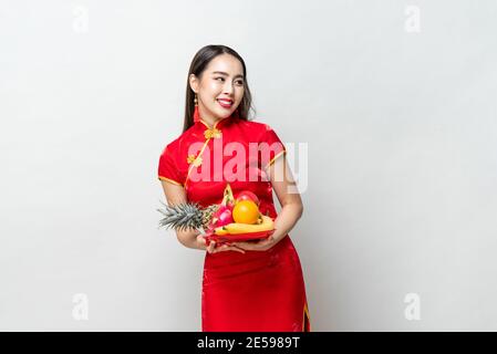 Junge asiatische Frau in traditinal rot cheongsam Kleid mit Glück Früchte für chinesisches Neujahr in hellgrau isoliert Studio Hintergrund Stockfoto