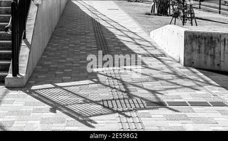 Schatten des Geländers der Betontreppe, ist auf einen Steinpflaster gegossen, in schwarz und weiß. Stockfoto