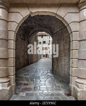 Eine Frau in der Ferne gesehen durch einen engen Torbogen in den alten Straßen von Kotor Altstadt. Stockfoto