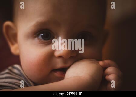 Zaehling bei Babys. Kleiner kaukasischer Junge hält seine Faust im Mund. Selektiver Fokus. Nahaufnahme des Fotos. Dunkle Tonung. Stockfoto