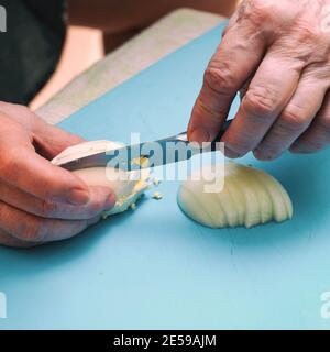 Frau schneidet mit einem Messer ein weißes gekochtes Ei auf Ein Schneidbrett in Stücke oder Scheiben für Salat Stockfoto