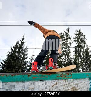 Rückansicht des gebeugten Snowboarders, der versucht, Balance zu halten, niedrige Winkelansicht. Sportler in farbenfrohem, lebhaftem Skianzug, roten Stiefeln und Snowboard. Konzept der Freeride Stockfoto