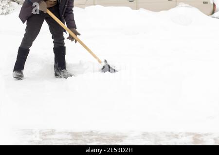 Ein Mann in Filzstiefeln, mit einer Schaufel in den Händen, entfernt nach einem Schneefall Schnee vom Bürgersteig. Stockfoto