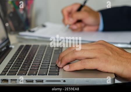Business man Hand tippt einen Computer und hält einen Stift Zum Schreiben von Geschäftsdokumenten auf dem Schreibtisch Stockfoto