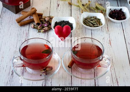Sorten von Kräutern in Glas Teekanne auf Holz vor der weißen Wand gebraut. Linden, Granatapfelblüte, grüner Tee, Traubenkern, Olivenblätter, Zimt-st Stockfoto