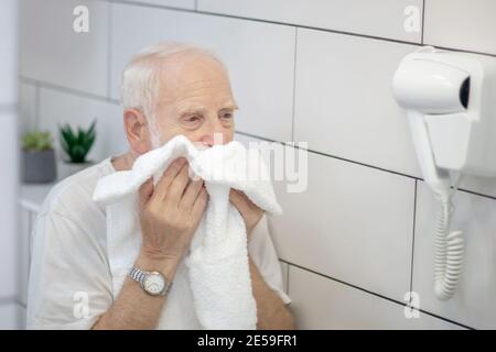 Grauhaariger Mann in weißem T-Shirt wischen sein Gesicht mit dem Handtuch Stockfoto