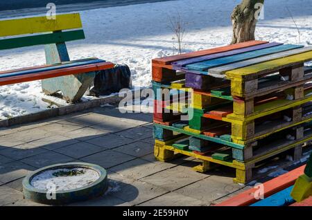 Modernes Street Art Konzept. Ein Sitzbereich auf einer Stadtstraße aus bunten Paletten. Bunte Bänke und Tisch. Sonniger Wintertag. Keine Personen. Stockfoto