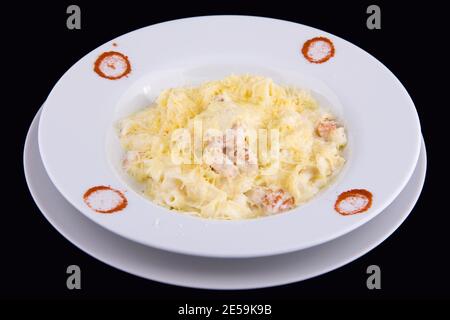 Fettuccine mit Lachs in Sahnesauce auf weißem Teller auf schwarzem Hintergrund. Stockfoto