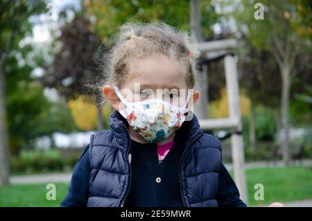 Kleine süßliche Mädchen tragen Masken gegen Staub und Viren zu schützen, ist die epidemische Zeit traurig und stressig. Selektiver Fokus im Gesicht. Stockfoto