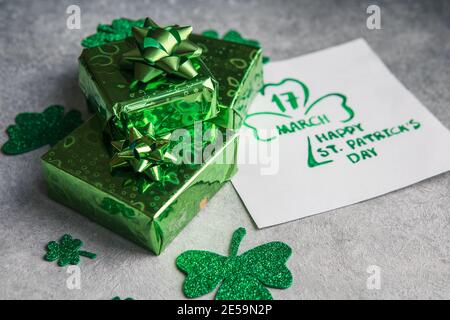 Dekorative Kleeblätter, grüne Geschenkschachtel, Münzen auf Steinhintergrund, flache Lage. St. Patrick's Day Feier. Karte Happy St. Patrick's Day Stockfoto