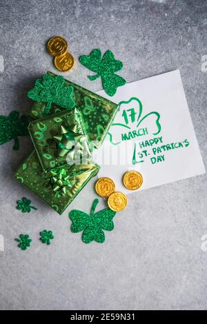 Dekorative Kleeblätter, grüne Geschenke, Münzen auf Steinhintergrund, flache Lage. St. Patrick's Day Feier Stockfoto