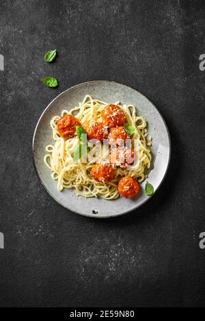 Spaghetti Pasta mit Fleischbällchen, Tomatensauce, geriebenem Käse und frischem Basilikum - gesunde hausgemachte italienische Pasta auf schwarzem Hintergrund, Draufsicht, Kopierraum Stockfoto