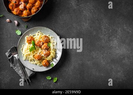 Spaghetti Pasta mit Fleischbällchen, Tomatensauce, geriebenem Käse und frischem Basilikum - gesunde hausgemachte italienische Pasta auf schwarzem Hintergrund, Draufsicht, Kopierraum Stockfoto