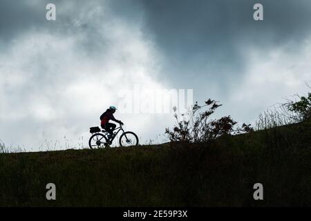 Silhouette Bild einer Radfahrerin auf dem Otago Central Rail Trail gegen den bewölkten Himmel, South Island, Neuseeland Stockfoto