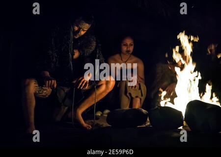 Horizontale Nahaufnahme eines Maori-Paares in traditioneller Kleidung, bei Nacht am Lagerfeuer, Mitai Maori Village, Rotorua, Neuseeland Stockfoto