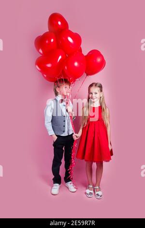 Valentinstag. Zwei glückliche Kinder mit herzförmigen Luftballons auf rosa Hintergrund. Zuerst Liebe Stockfoto
