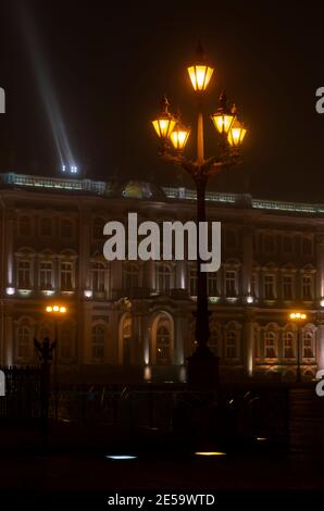 Laternen im selektiven Fokus im Vordergrund und verschwommener Hintergrund mit einem Winterpalast mit Nachtbeleuchtung (St. Petersburg, Russland) Stockfoto