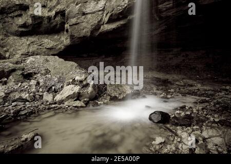 Monochromatisches Bild des kleinen Wasserfalls vor der Kalksteinhöhle im Lahemaa Nationalpark, Estland Stockfoto