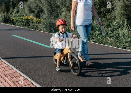 Kind fährt mit dem Laufrad auf einem Fahrradweg. Mutter und Sohn auf dem morgendlichen Schulweg. Stockfoto