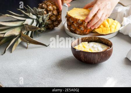 Gesundes Frühstückssaft, Joghurt mit frischer Mango und Ananas in der Kokosnussschale Stockfoto