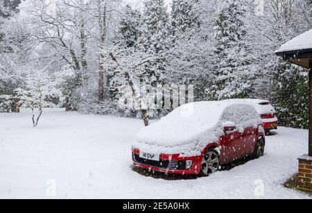 Ein rotes Volkswagen Golf GTI-Auto, das während eines starken Schneefalls im Winter in einer Vorstadtfahrt geparkt wurde: Woking, Surrey, Südostengland Stockfoto