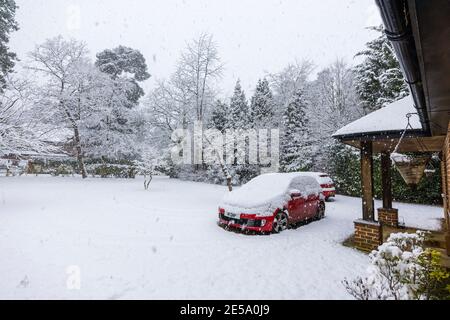 Ein rotes Volkswagen Golf GTI-Auto, das während eines starken Schneefalls im Winter in einer Vorstadtfahrt geparkt wurde: Woking, Surrey, Südostengland Stockfoto