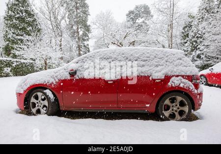 Ein rotes Volkswagen Golf GTI-Auto, das während eines starken Schneefalls im Winter in einer Vorstadtfahrt geparkt wurde: Woking, Surrey, Südostengland Stockfoto