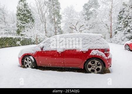 Ein rotes Volkswagen Golf GTI-Auto, das während eines starken Schneefalls im Winter in einer Vorstadtfahrt geparkt wurde: Woking, Surrey, Südostengland Stockfoto