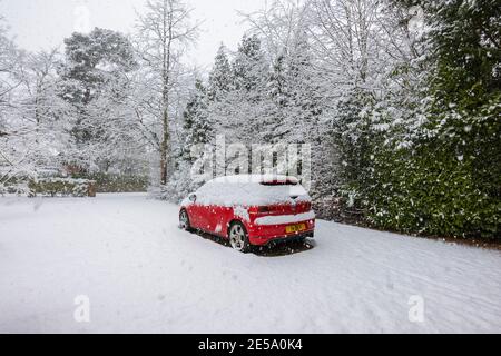 Ein rotes Volkswagen Golf GTI-Auto, das während eines starken Schneefalls im Winter in einer Vorstadtfahrt geparkt wurde: Woking, Surrey, Südostengland Stockfoto