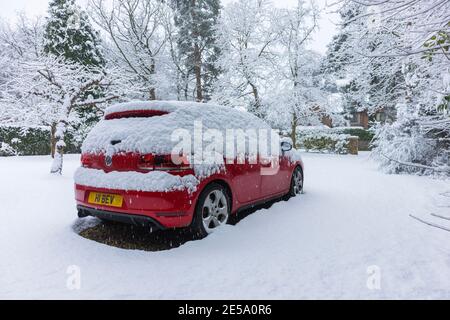 Ein rotes Volkswagen Golf GTI-Auto, das während eines starken Schneefalls im Winter in einer Vorstadtfahrt geparkt wurde: Woking, Surrey, Südostengland Stockfoto