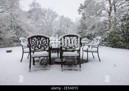 Tische und Stühle im Freien auf einer Terrasse und Bäume, die bei starkem Schneefall in einem Vorstadtgarten Woking, Surrey, Südostengland, bedeckt sind Stockfoto