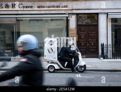 Während der Corona Virus Epidemie, Bond Street, London, erwartet ein Fahrer mit Lebensmittelzustellung auf einem Roller seinen nächsten Job. Stockfoto